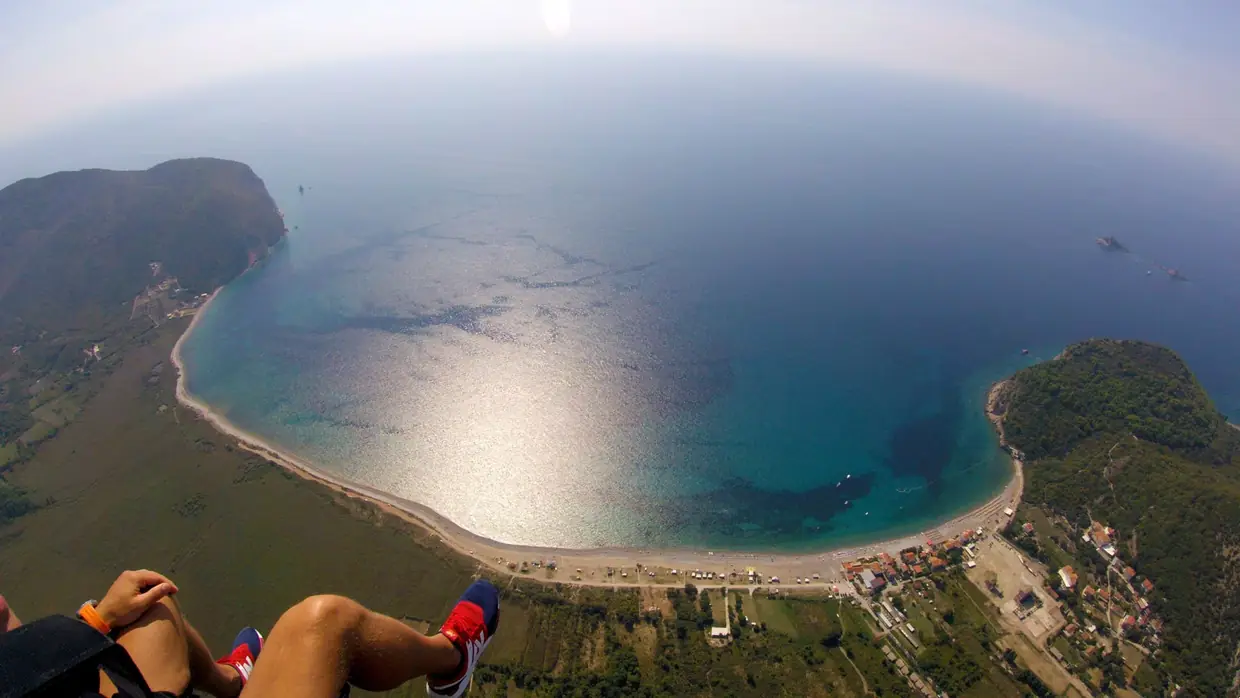 Paragliding over a wide Montenegro bay with sunlit water and coastal mountains.
